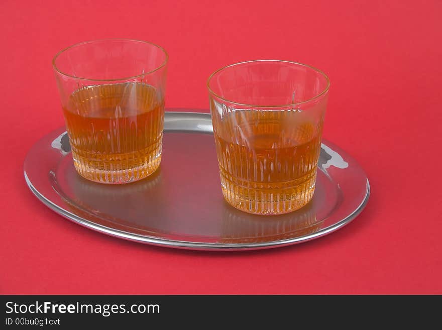 Two glasses with whiskey standing on a silver tray on red backgorund. Two glasses with whiskey standing on a silver tray on red backgorund