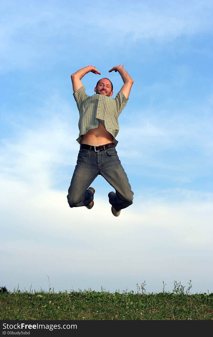 A man jumping over grass with a blue sky behind him