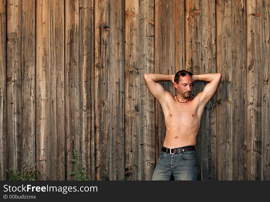 An athletic muscular young man in jeanes leaning against a rustical wooden wall. An athletic muscular young man in jeanes leaning against a rustical wooden wall.