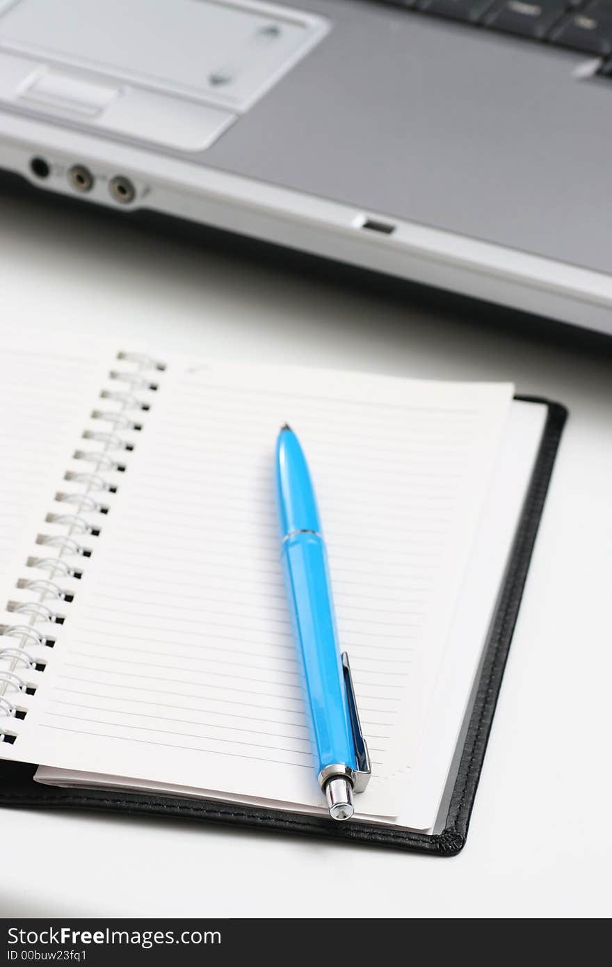 Blue pen on notebook and laptop computer in background