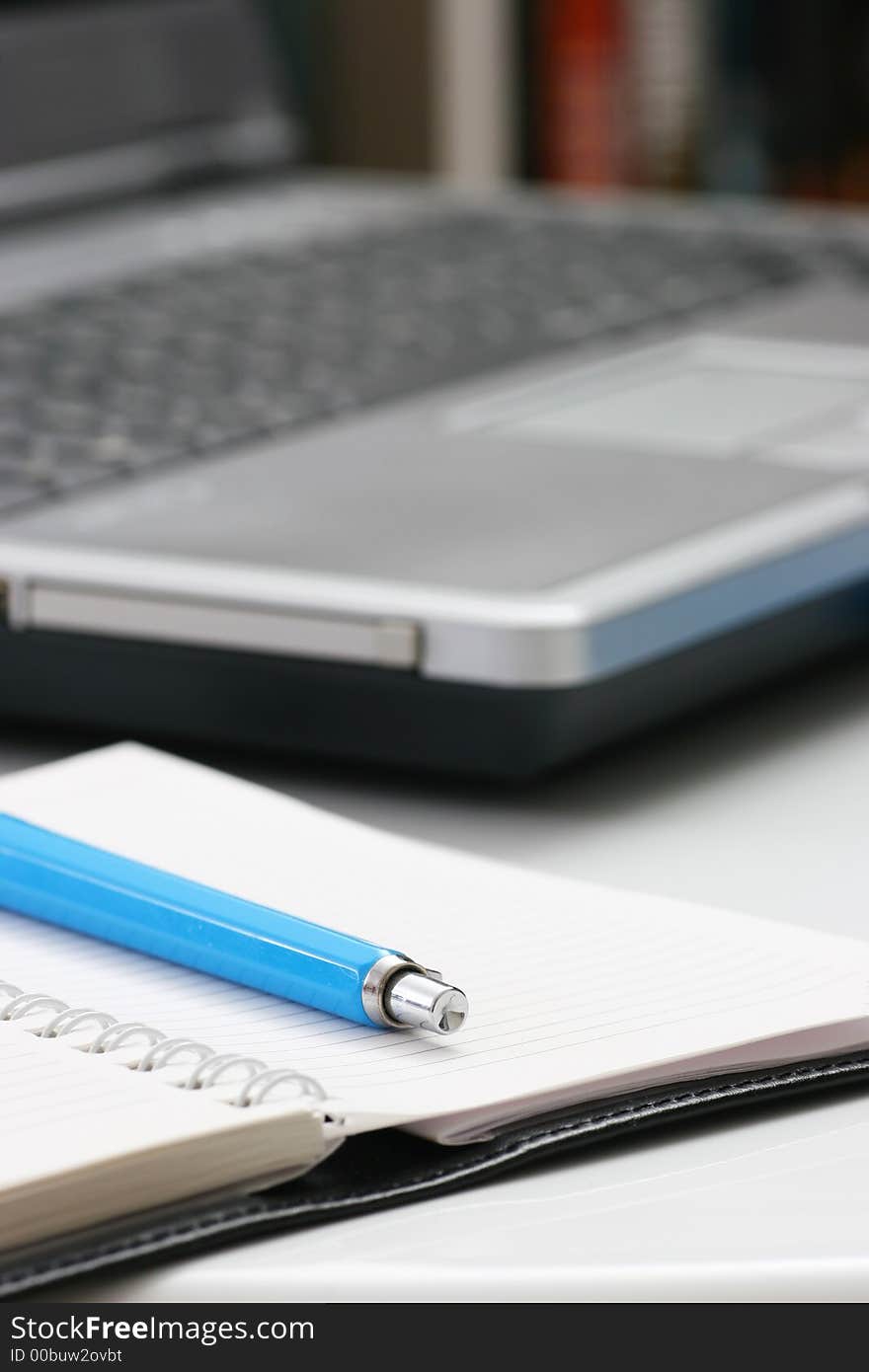 Blue pen on notebook and laptop computer in background