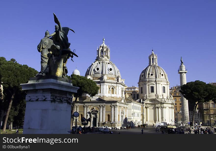 Monumental domes of the church on piazza Venezia with forum column and sculpture of the national monument