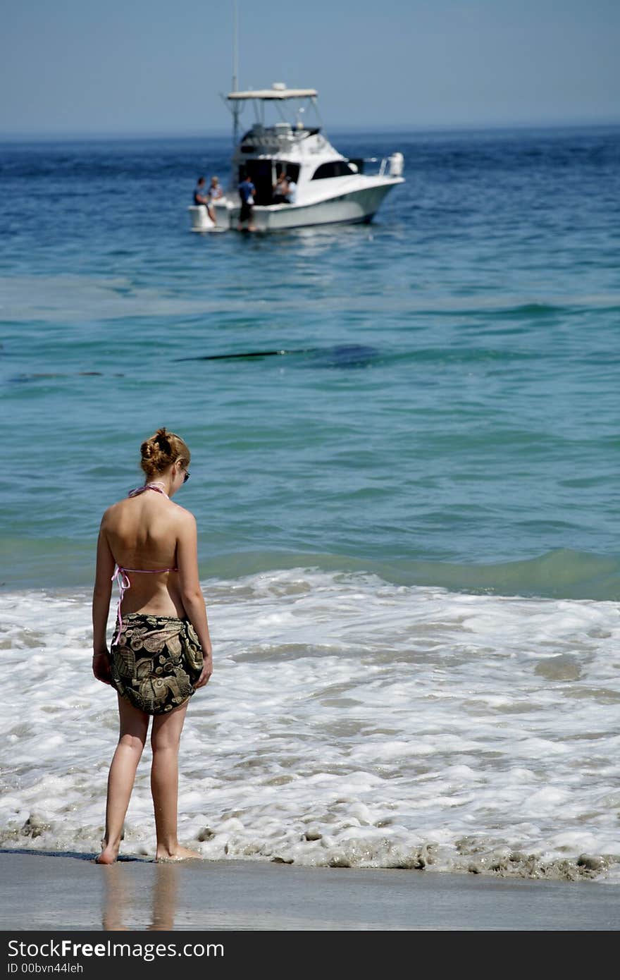 A woman standing in waves with boat in background. A woman standing in waves with boat in background