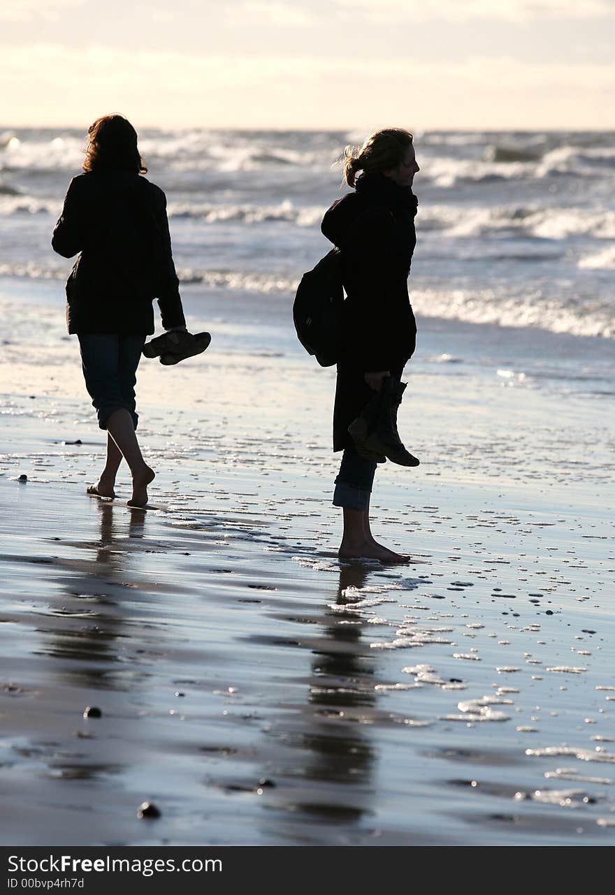 Two girlfriends barefoot go on wet sand. Two girlfriends barefoot go on wet sand