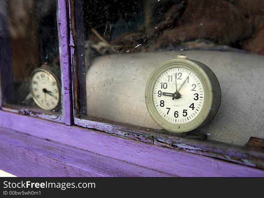 Old clocks are behind a window of a dilapidated house