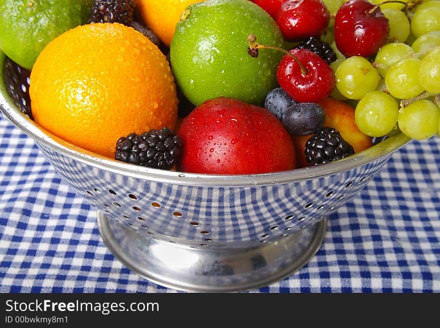 Freshly washed fruits drain in a stainless steel colander.