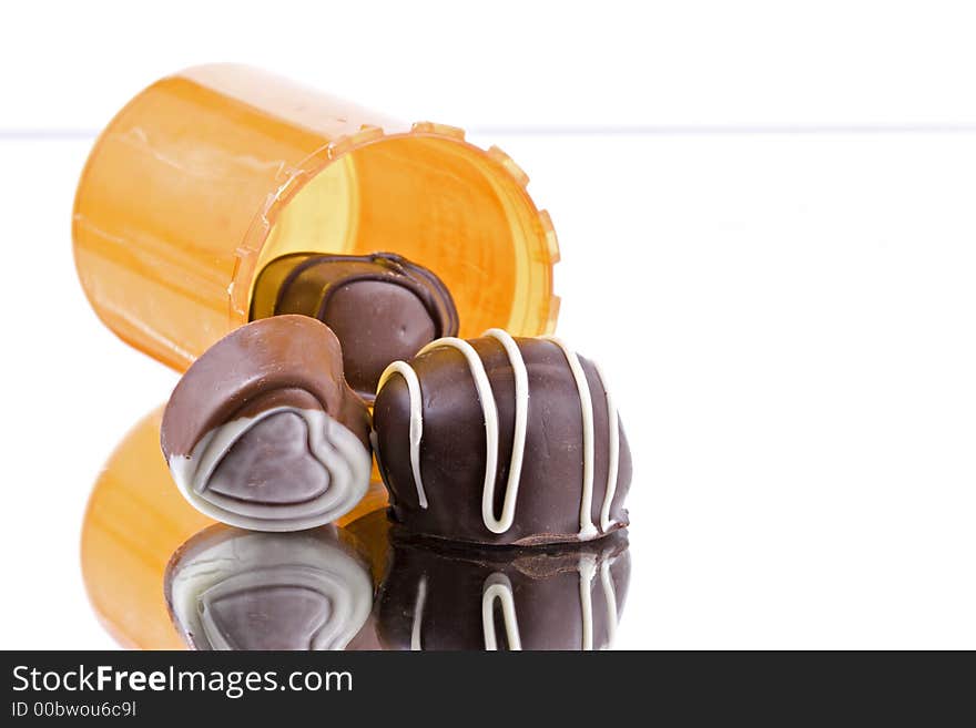 Prescription medication bottle on side with three pieces of chocolates outpouring from bottle with white background and reflected on mirror. Prescription medication bottle on side with three pieces of chocolates outpouring from bottle with white background and reflected on mirror