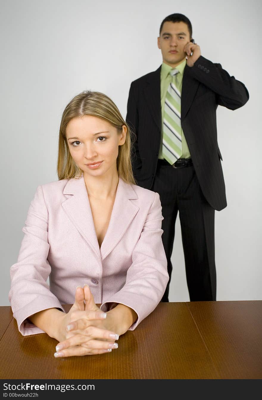 Woman's sitting at the office desk. Man's standing behind her and talking mobile phone. Woman's sitting at the office desk. Man's standing behind her and talking mobile phone.