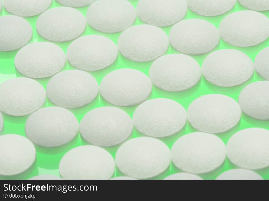 Round white pills sit on a bright green table. Round white pills sit on a bright green table.