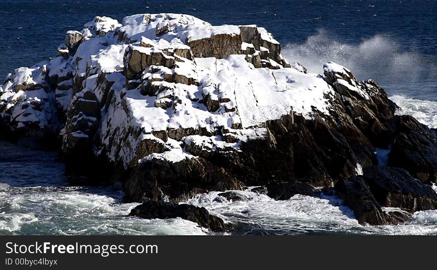 Snow covered rocks in the ocean with waves crashing