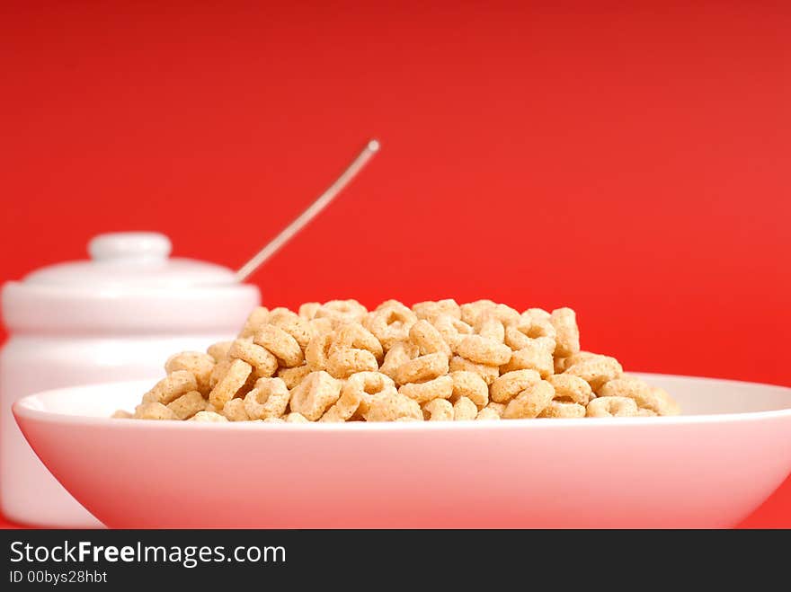 A bowl of oat cereal with sugar bowl on red background