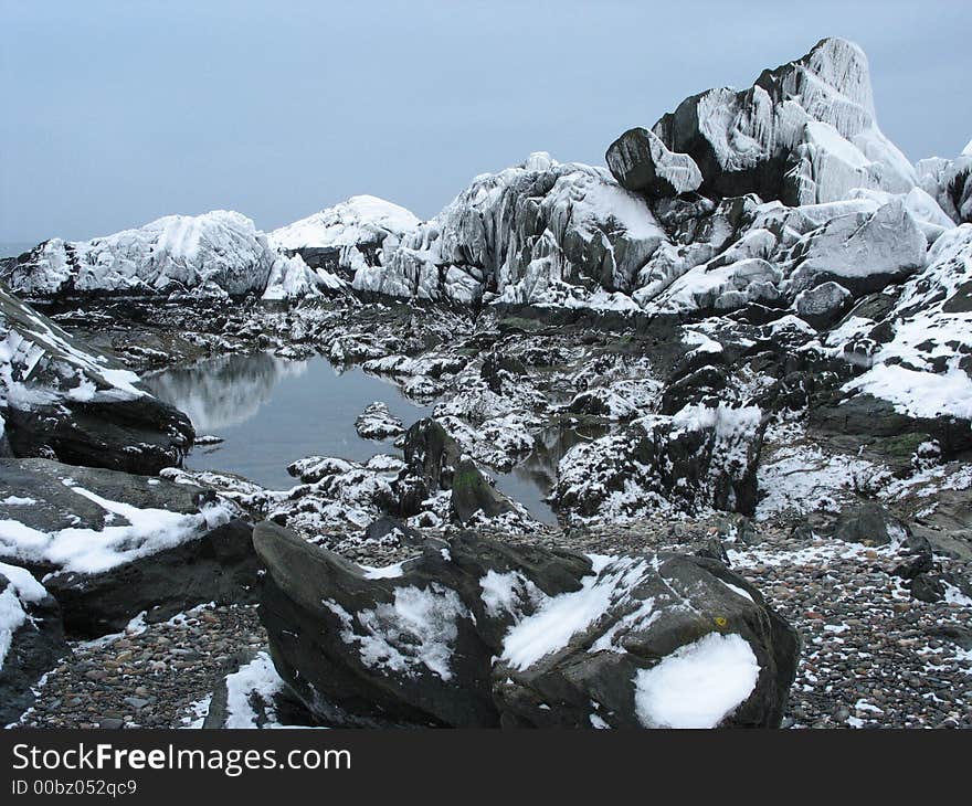 Snow-covered rocks at low tide, and a small tidal pool on the shore of the Atlantic ocean