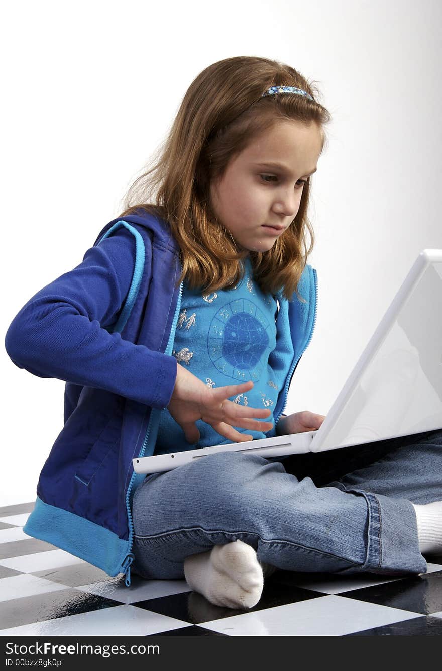 Grade school age girl working on a white laptop computer while sitting crosslegged on the floor. Grade school age girl working on a white laptop computer while sitting crosslegged on the floor.