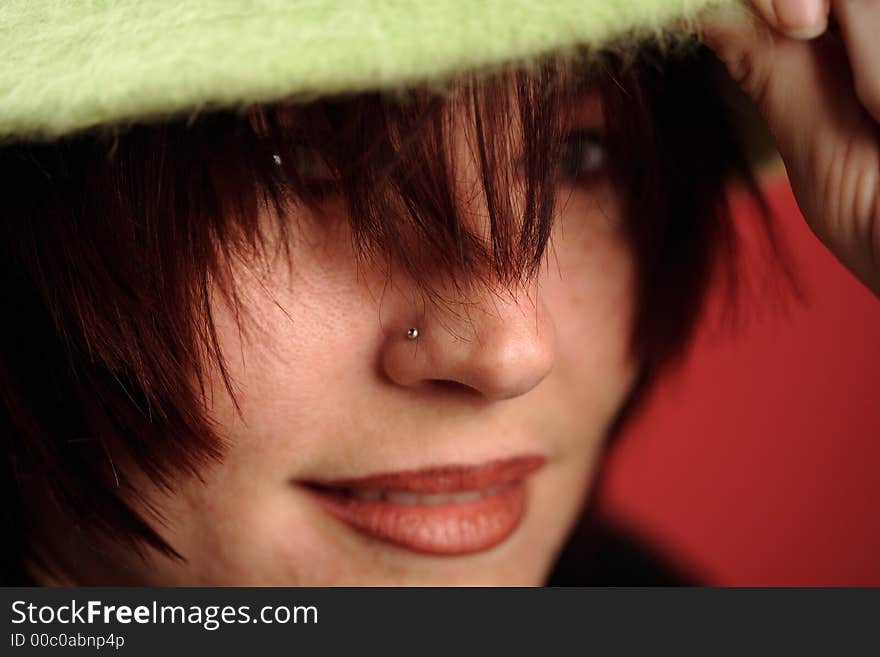 A portrait of a cute read headed woman with a green hat on red background. The woman is smiling and holding her hand up to her hat. A portrait of a cute read headed woman with a green hat on red background. The woman is smiling and holding her hand up to her hat.