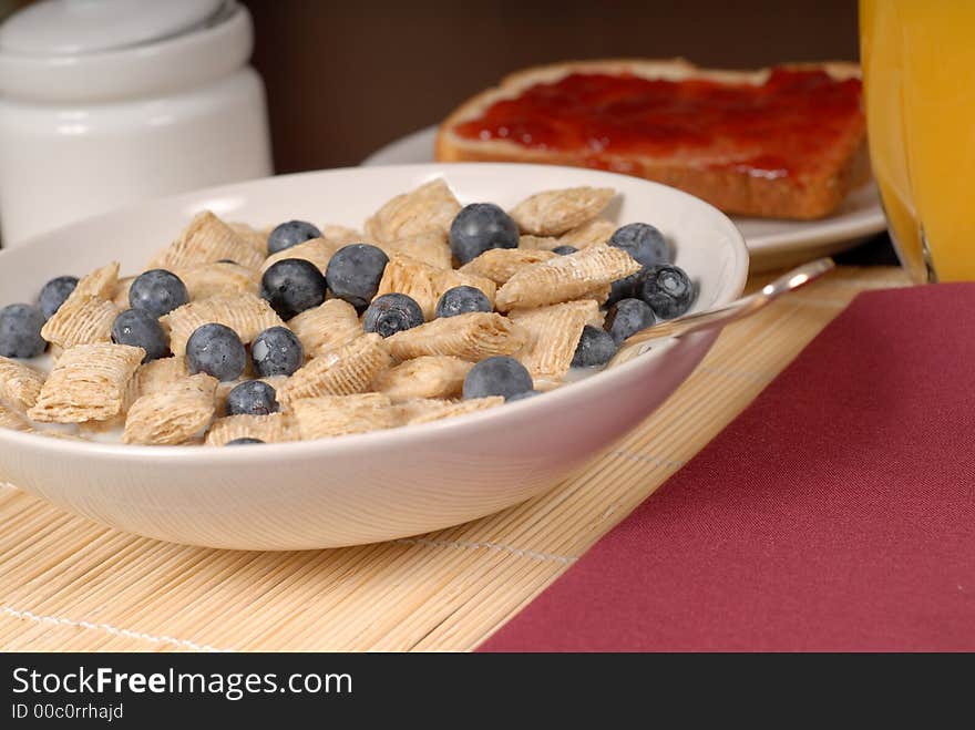 A bowl of wheat cereal with blueberries, toast and orange juice