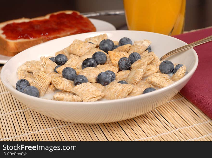 A bowl of wheat cereal with blueberries, toast and orange juice