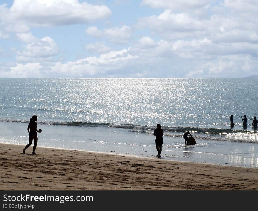 Beach landscape at sunrise with people playing near the sea