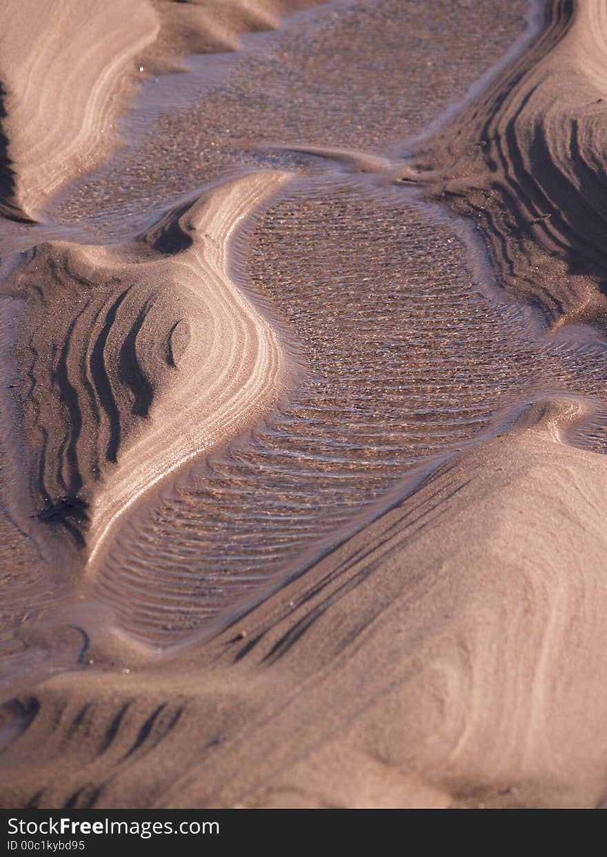 Sand sculptured by the sea leave ripple images on the sand, amongst a puddle of sea water. Sand sculptured by the sea leave ripple images on the sand, amongst a puddle of sea water.