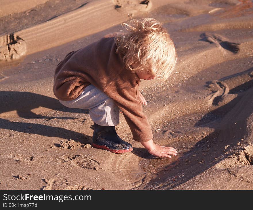 A small boy plays at the beach in a sandy beach puddle. Totally immersed in what he is doing. A small boy plays at the beach in a sandy beach puddle. Totally immersed in what he is doing.