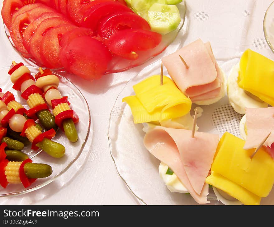 Piece of holiday supper table: tomato,cucumber,pickled cucumbers,cork,red paprika,onion,fungus,egg,cheese,ham on the plates,tablecloth