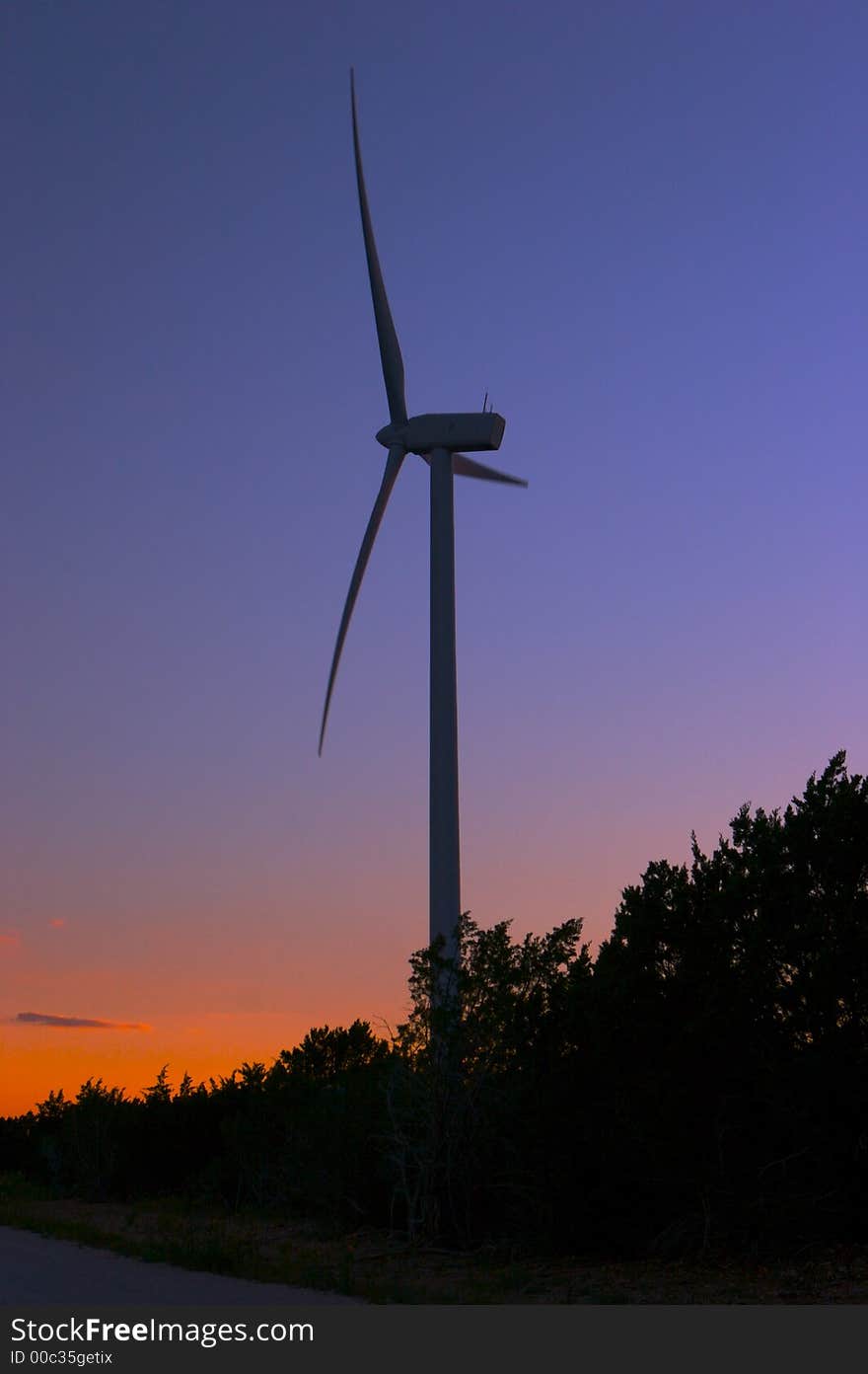 Wind farm at dusk with trees in shadows