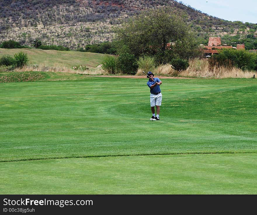 Golfer on the South African golf course pitching the ball onto the green. Golf club is in motion and the ball is in the air. Golfer on the South African golf course pitching the ball onto the green. Golf club is in motion and the ball is in the air.