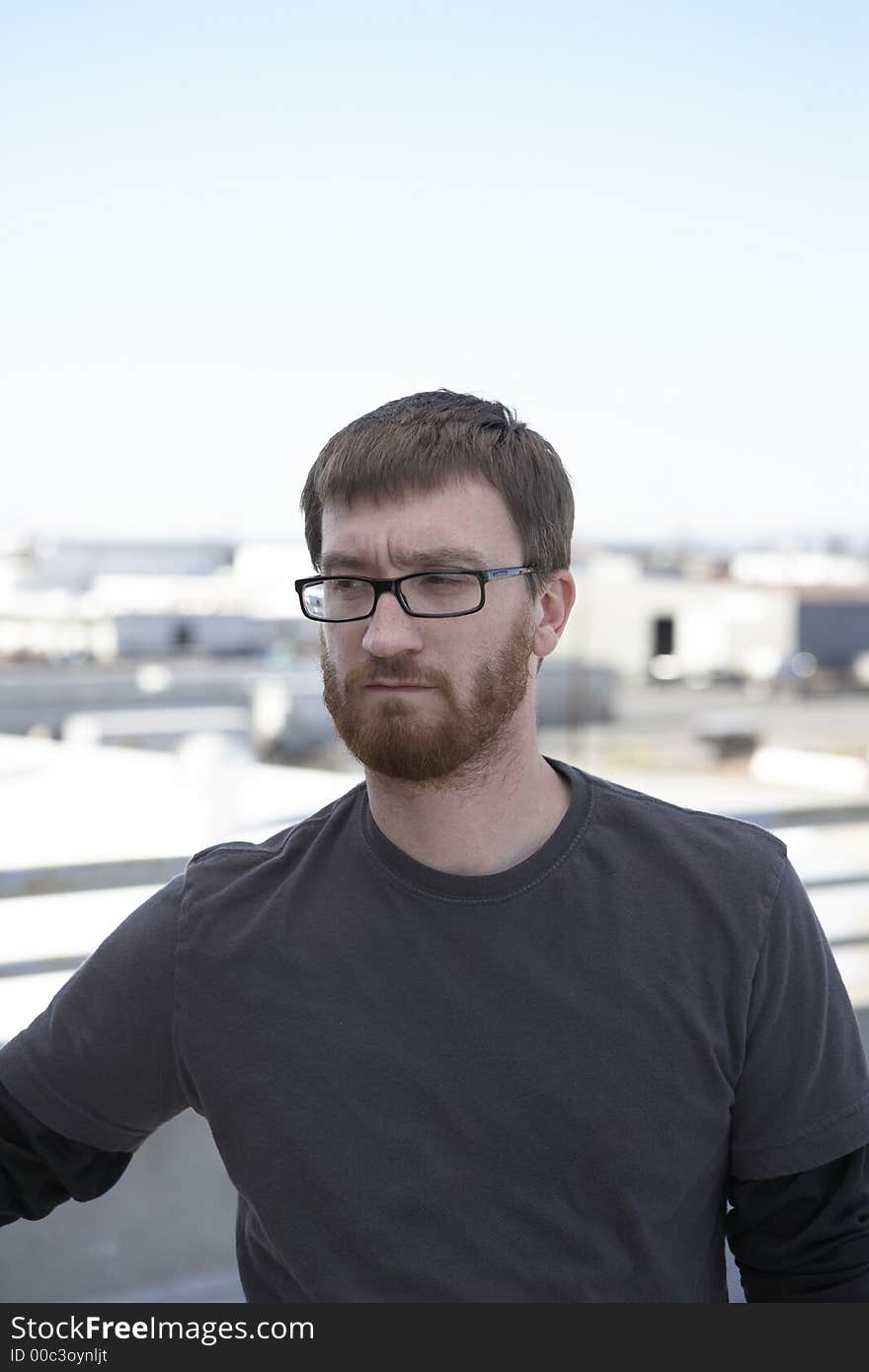 Man wearing tee shirt standing on the roof with city in the background. Man wearing tee shirt standing on the roof with city in the background.