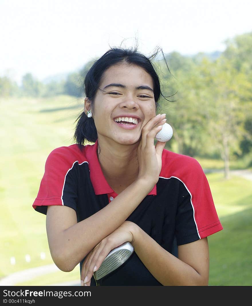 Yeoung, female golf player smiling, holding golf club and ball, with fairway in the background. Yeoung, female golf player smiling, holding golf club and ball, with fairway in the background.