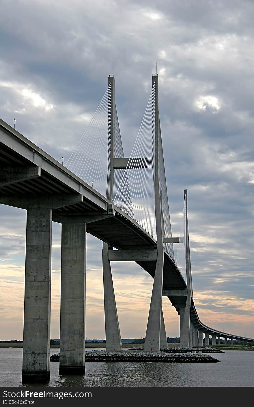 Concrete and suspension bridge spanning a waterway backed by clouds. Concrete and suspension bridge spanning a waterway backed by clouds