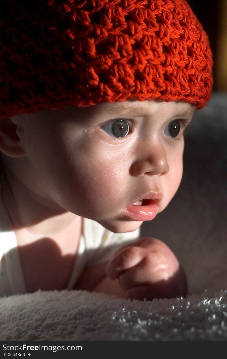 Image of baby wearing a red crochet cap, lying on a bed, lit by the setting sun. Image of baby wearing a red crochet cap, lying on a bed, lit by the setting sun