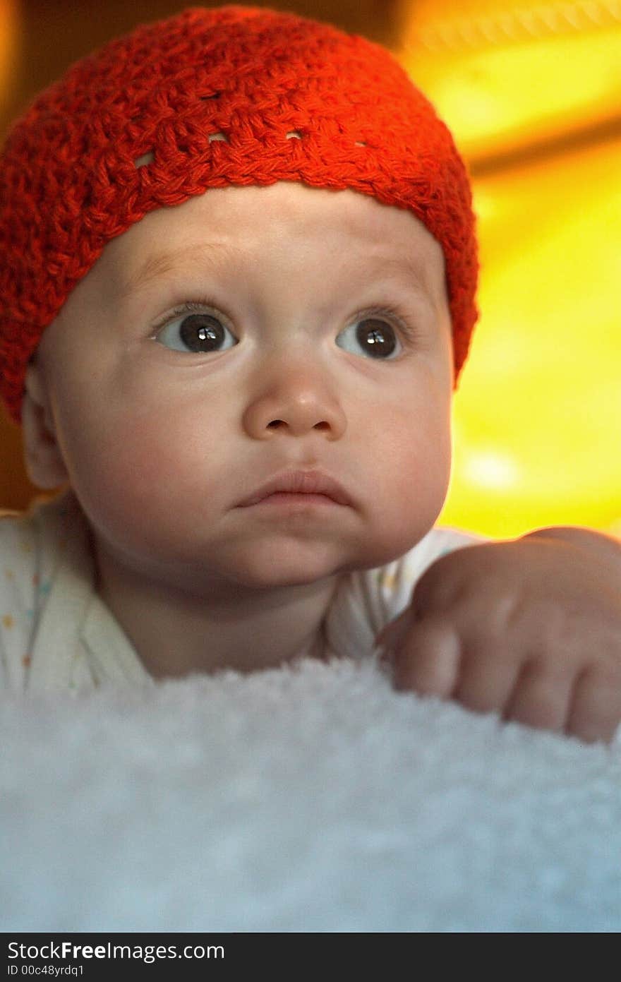 Image of baby wearing a red crochet cap, lying on a bed, lit by the setting sun. Image of baby wearing a red crochet cap, lying on a bed, lit by the setting sun