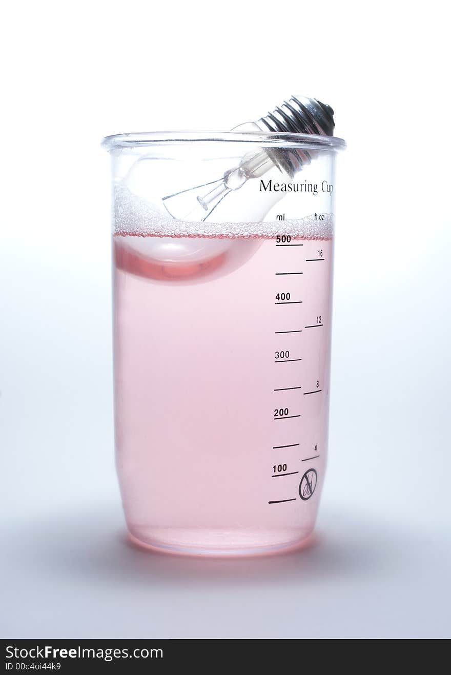 Lamp in rose liquid in measuring cup on white. Lamp in rose liquid in measuring cup on white