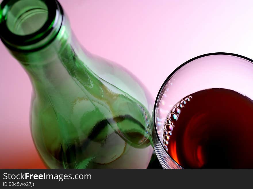 Green wine bottle and glass of red wine against pinkish white background. Green wine bottle and glass of red wine against pinkish white background.