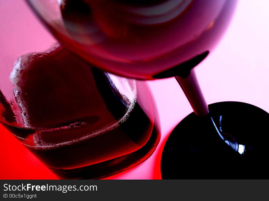 Clear wine bottle and glass of red wine against pinkish white background. Clear wine bottle and glass of red wine against pinkish white background.