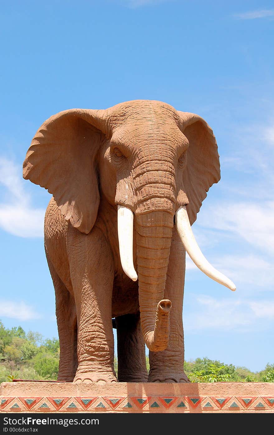 Elephant- whitish tusks-brown body-sculpture-pedestal. Elephant- whitish tusks-brown body-sculpture-pedestal