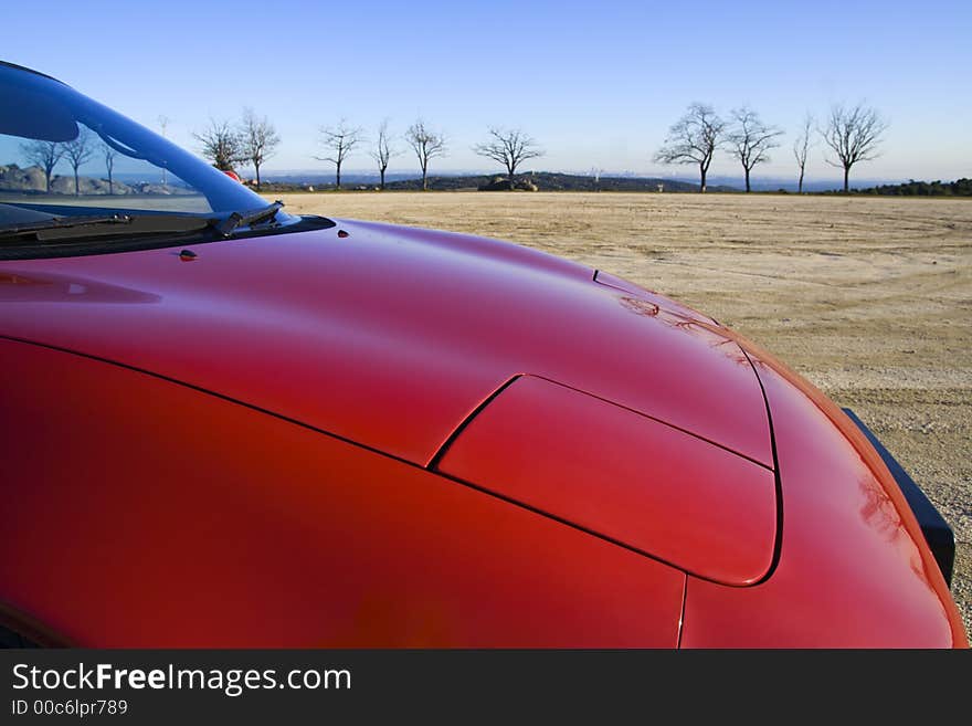 Nose of a classic red sports car on a dust track with perfect blue sky. Nose of a classic red sports car on a dust track with perfect blue sky.