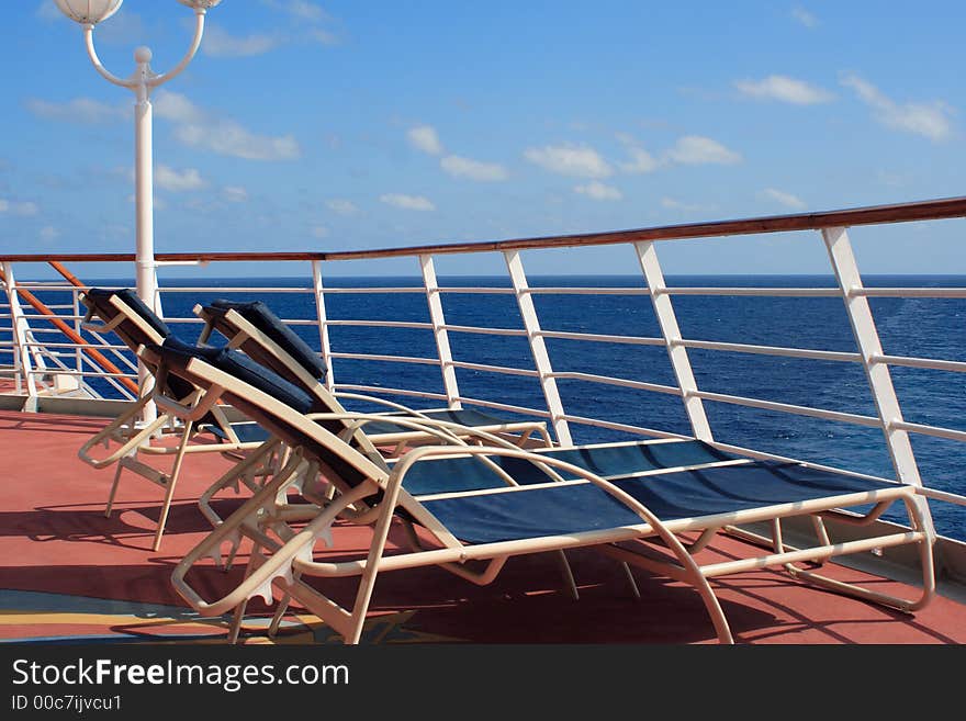 Lounge chairs overlooking the blue ocean behind the railing on a vacation cruise ship. Lounge chairs overlooking the blue ocean behind the railing on a vacation cruise ship.