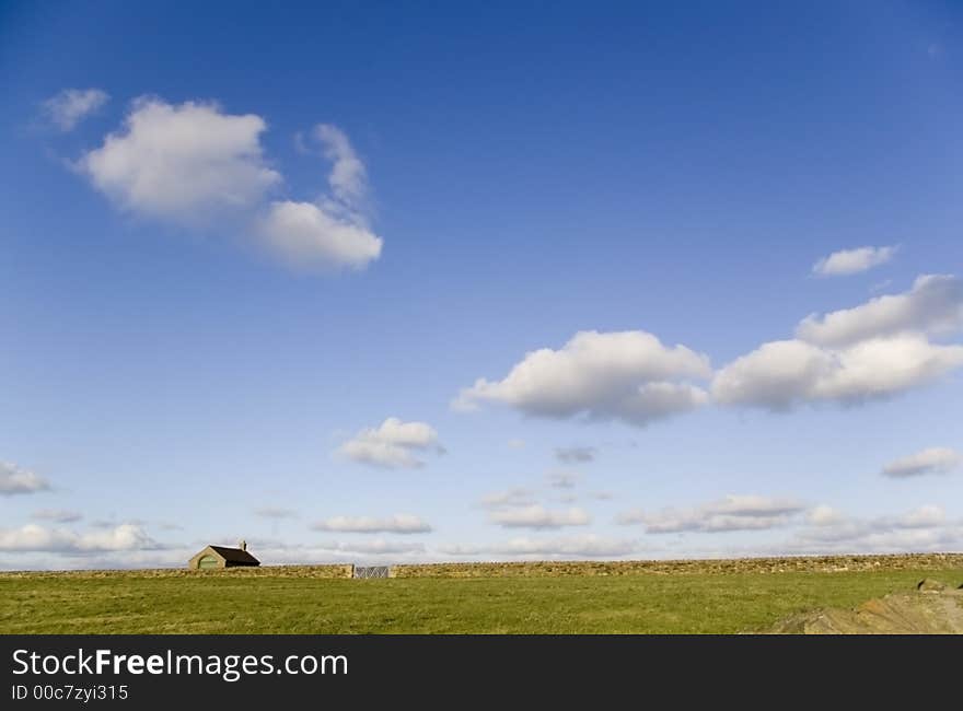 A lonely house on a stretch of green grass under a blue sky with white couds. A lonely house on a stretch of green grass under a blue sky with white couds.