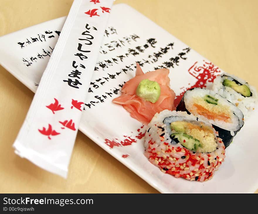 Pieces of sushi (sashimi) on a white plate with Japanese (kanji) writing. Includes chopsticks, wasabi paste and pickled ginger. Close Up. Pieces of sushi (sashimi) on a white plate with Japanese (kanji) writing. Includes chopsticks, wasabi paste and pickled ginger. Close Up.