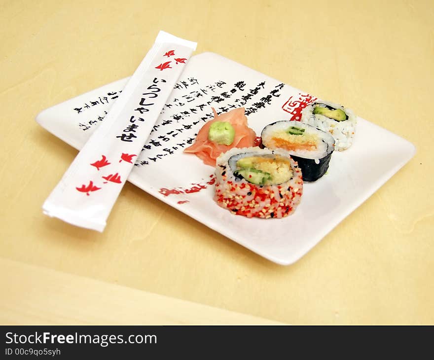 Pieces of sushi (sashimi) on a white plate with Japanese (kanji) writing. Includes chopsticks, wasabi paste and pickled ginger. Close Up. Pieces of sushi (sashimi) on a white plate with Japanese (kanji) writing. Includes chopsticks, wasabi paste and pickled ginger. Close Up.