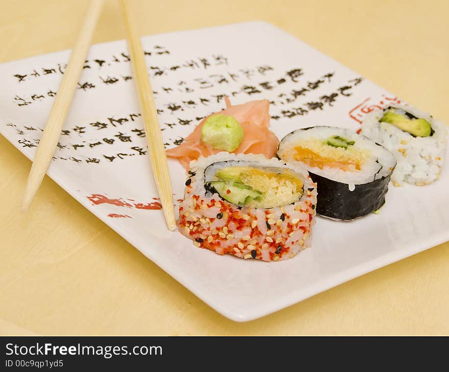 Pieces of sushi (sashimi) on a white plate with Japanese (kanji) writing. Includes chopsticks, wasabi paste and pickled ginger. Close Up. Pieces of sushi (sashimi) on a white plate with Japanese (kanji) writing. Includes chopsticks, wasabi paste and pickled ginger. Close Up.