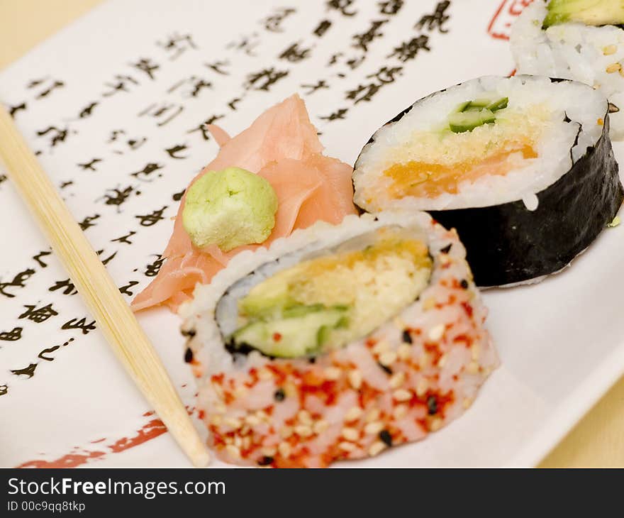 Pieces of sushi (sashimi) on a white plate with Japanese (kanji) writing. Includes chopsticks, wasabi paste and pickled ginger. Close Up. Pieces of sushi (sashimi) on a white plate with Japanese (kanji) writing. Includes chopsticks, wasabi paste and pickled ginger. Close Up.