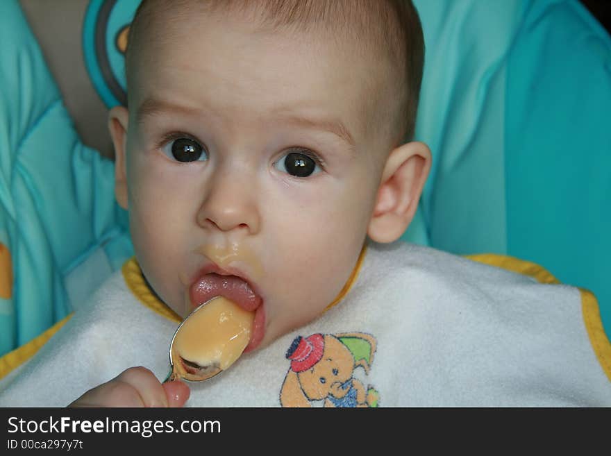 The kid of 7 months sits with the spoon. The kid of 7 months sits with the spoon