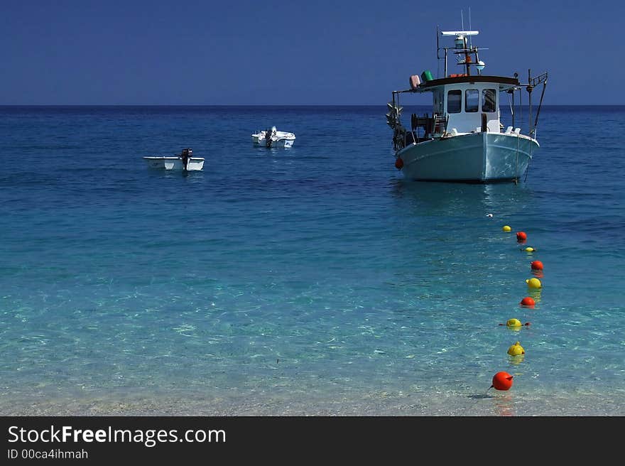 Three boats at sea with blue sky and color buoy.