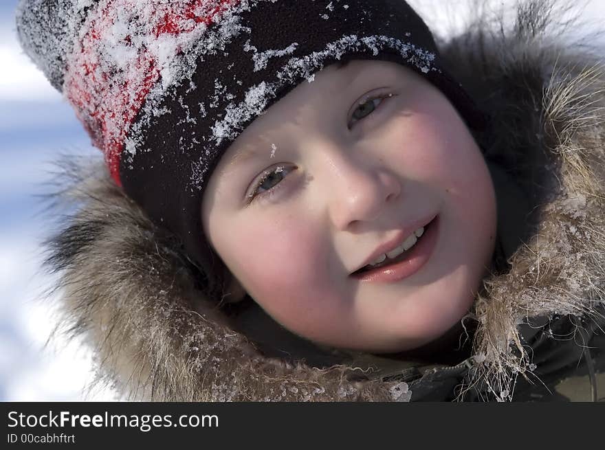 Portrait of young smiling boy in winter clothes and hat covered with snow taken in sunny, cold winter day. Portrait of young smiling boy in winter clothes and hat covered with snow taken in sunny, cold winter day