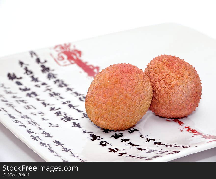 Two Lychee (litchi) placed on a white plate with Japanese (kanji) writing. Close Up. Two Lychee (litchi) placed on a white plate with Japanese (kanji) writing. Close Up.