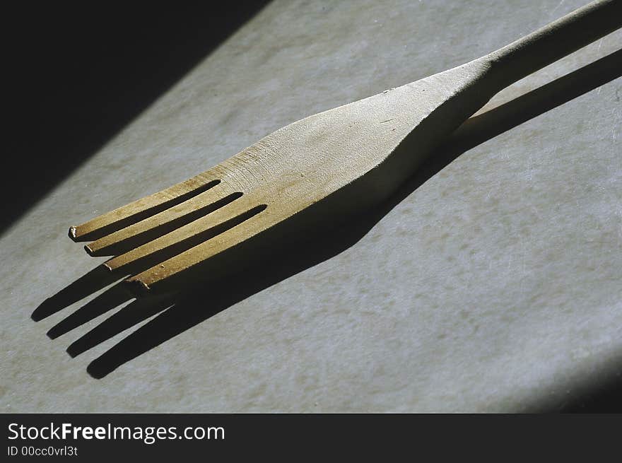 A wooden fork utensil used for cooking sitting on a counter in the sunlight.