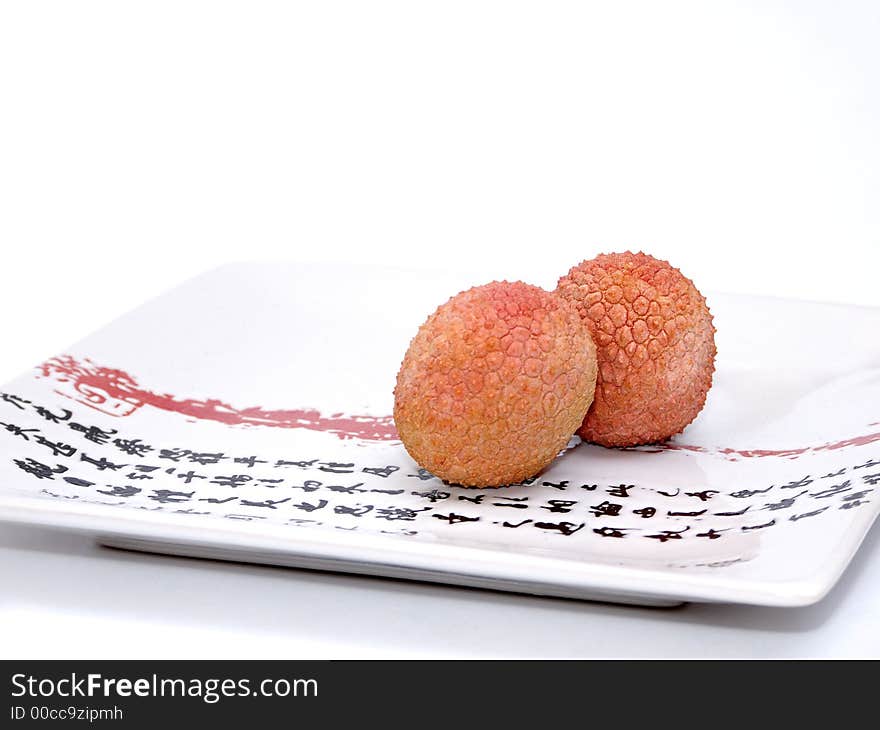 Two Lychee (litchi) placed on a white plate with Japanese (kanji) writing. Close Up. Two Lychee (litchi) placed on a white plate with Japanese (kanji) writing. Close Up.