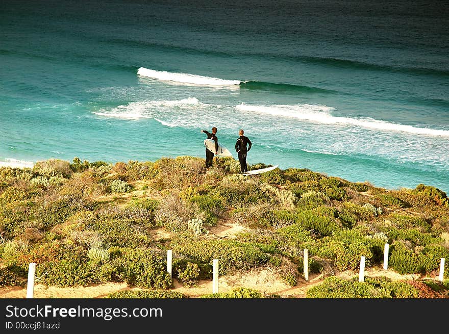 Surfers stand on top of sand hill and contenplate waves. Surfers stand on top of sand hill and contenplate waves