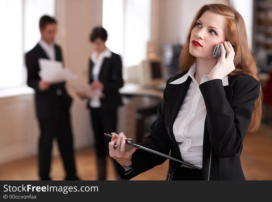 Businesswoman is talking on the phone and her colleagues are standing in the back. Businesswoman is talking on the phone and her colleagues are standing in the back